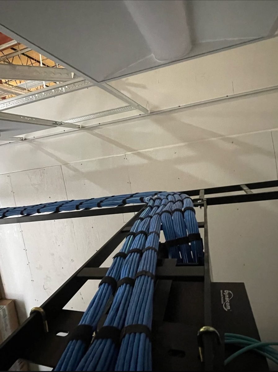 Blue Cat6 cable bundles combed and strapped along overhead ladder rack dropping into a network rack in a new construction commercial building, installed by DataTel 360