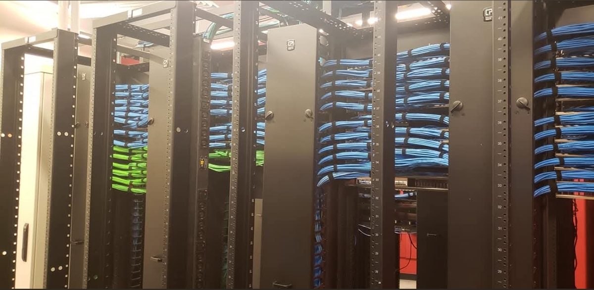 Row of open-frame network racks in an enterprise data center with blue and green patch cabling dressed across horizontal managers, installed by DataTel 360