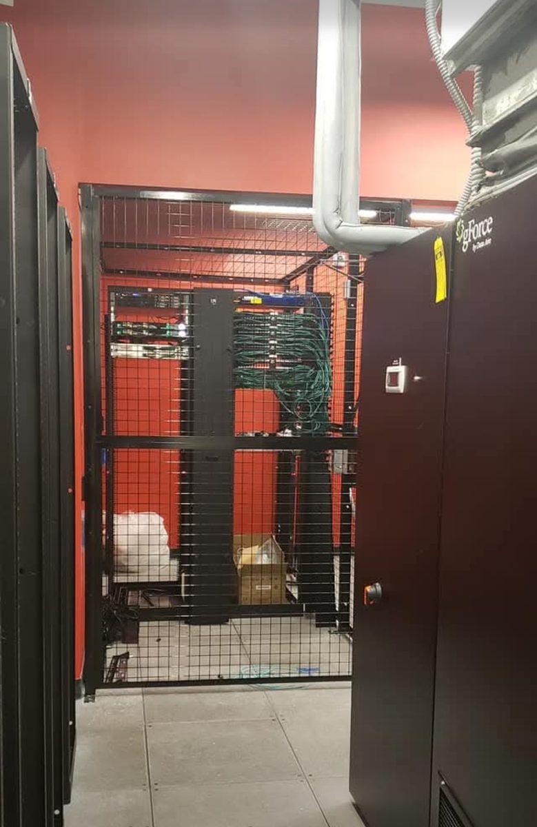 Secure caged equipment enclosure in a data center containing network racks and cabling, with precision cooling equipment alongside, supported by DataTel 360