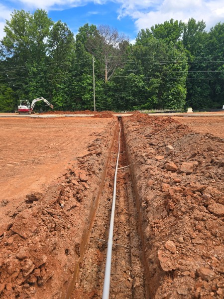 Open trench with underground conduit installed for a future building-to-building fiber pathway at a commercial construction site in Jefferson, Georgia