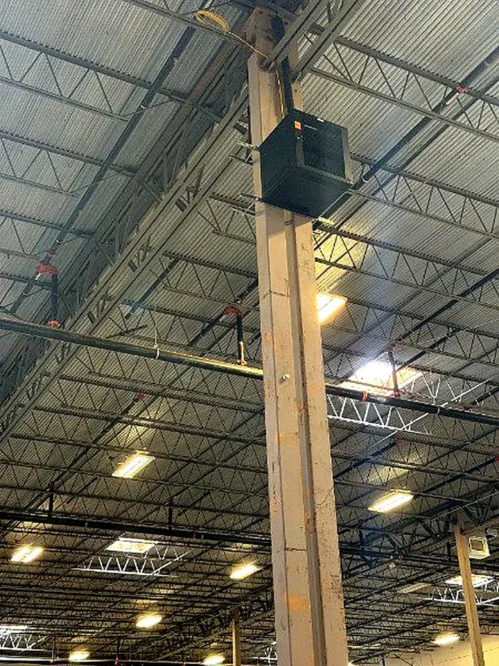 Enclosure mounted high on a steel column in a high-bay warehouse, with cabling run up the column